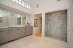 Master bathroom, marble tiled, high glass block windows allow for natural light, double vanity, full length mirror, jetted tub with hand sprayer, built-in shelving, walk-in shower with double shower heads, glass doors, linen closet, and modern fixtures.