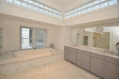 Master bathroom, marble tiled, high glass block windows allow for natural light, double vanity, full length mirror, jetted tub with hand sprayer, built-in shelving, walk-in shower with double shower heads, glass doors, linen closet, and modern fixtures.