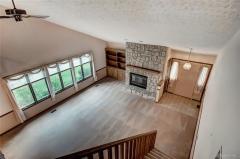 View of living room with stone fireplace and built-ins from loft area